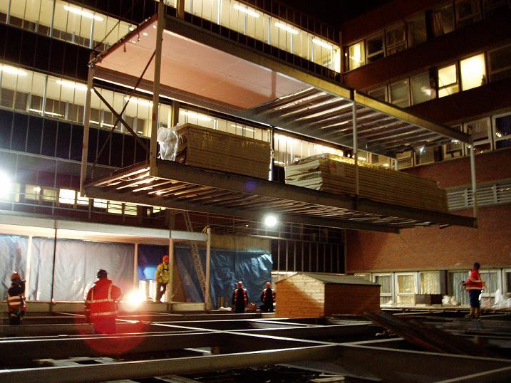 One of the fourteen modular steel cleanroom frames is lifted carefully over the six-story hospital wing. Work continued at night to minimise disruption to hospital services, and achieve a quick completion.