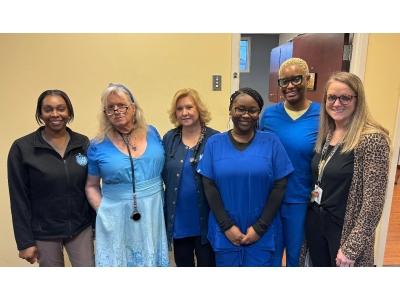 A group of six diverse women, likely a medical or clinical team, are posed together in a professional setting.