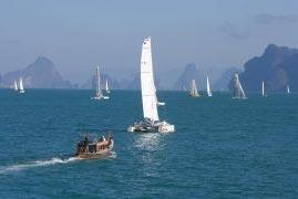 A Thai longtail boat following the fleet through the open waters of Phang Nga Bay with a view of limestone islands.