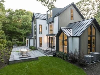 A contemporary home with sleek lines, large windows, and a spacious outdoor patio, surrounded by lush greenery. The dark metal roof contrasts beautifully with the light exterior.