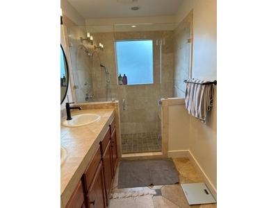 A well-lit bathroom features a glass-enclosed shower with beige tiles, a double vanity with a sleek black faucet, and a soft, neutral color palette for a calming atmosphere.