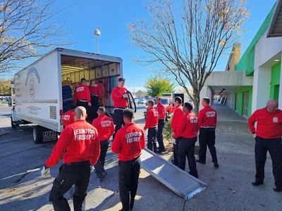 A team from Firefighters Move U is actively unloading a moving truck, wearing matching red Lexington Fire Dept. shirts. Their teamwork and organized effort highlight their commitment to providing professional and reliable moving services.