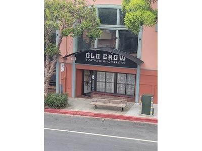 Street view of Old Crow Tattoo and Art Gallery, featuring its black storefront sign and a sidewalk bench in front of a windowed facade.