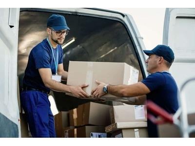 An image of two movers in blue uniforms handing a cardboard box out of the back of a moving van, highlighting the dependable service from Daymakers Moving & Storage, professional local movers hudson residents depend on.