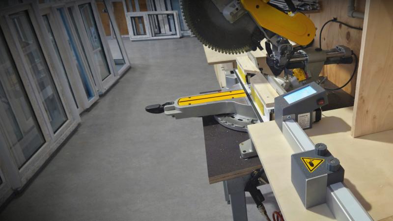 Pedante automatic length stop installed on a miter saw for precise, repeatable cutting in a PVC window production workshop.