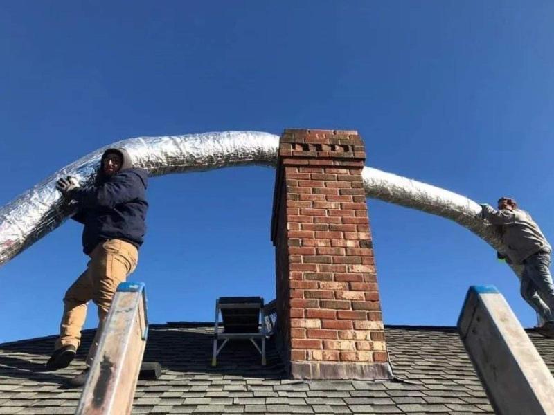 Neighborhood Chimney Services technicians feeding a stainless chimney liner into a brick chimney