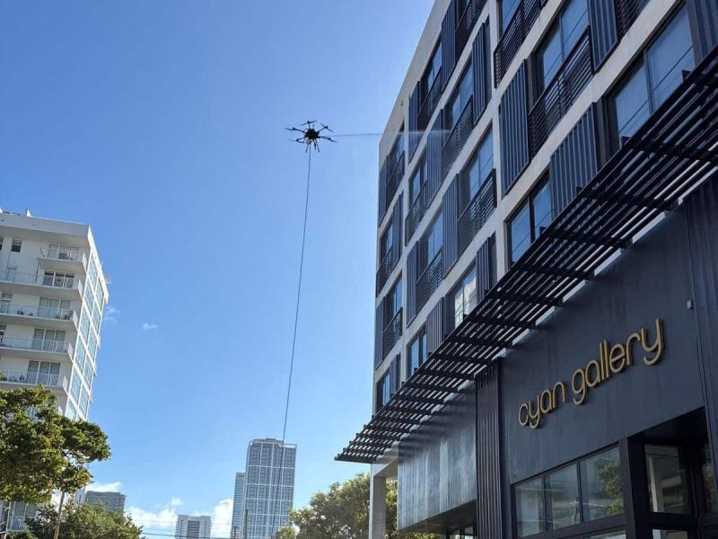 A tethered cleaning drone washes the upper windows of Sentral Wynwood above a street-level gallery in Miami