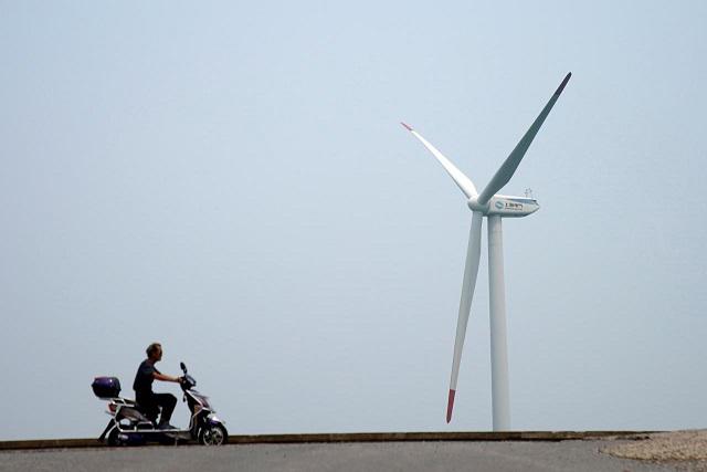 A man rides an electric scooter past a wind turbine in Shanghai, China August 11, 2017. REUTERS/Aly Song