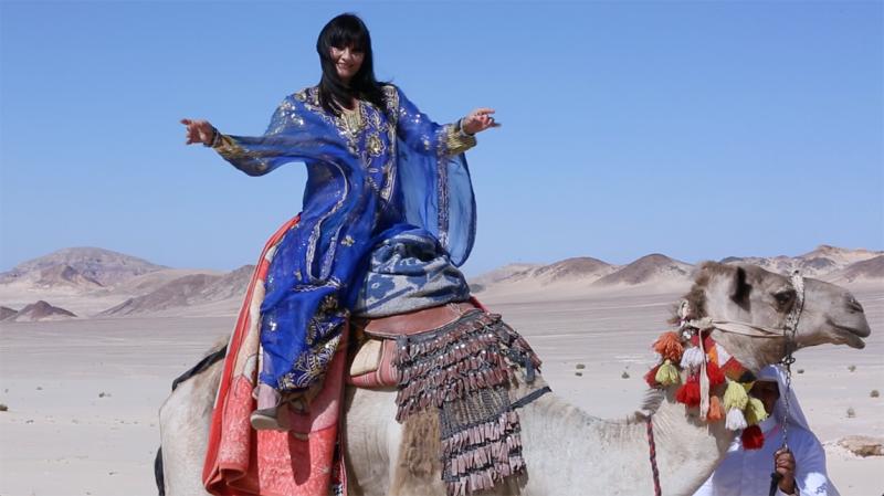 Lady Volcano sitting on a camel during the shooting of "Welcome to Qatar"
