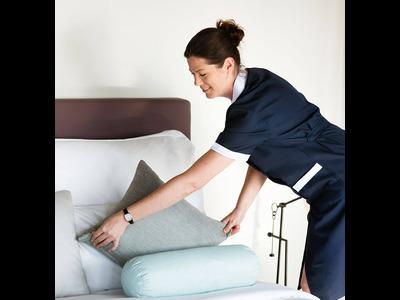 An image capturing a woman from Limpia Cleaning Services standing near a neatly made bed. She faces the bed with a professional demeanor, ready to provide expert cleaning services. The scene reflects the company's commitment to delivering quality results