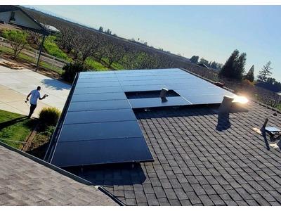 A solar panel array on a shingled roof with a worker, in a rural or suburban setting under a clear sky from Spartan Home Services.