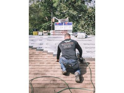 GutterHawk employee installing shingles on a roof, with roofing materials nearby, in Tallahassee.