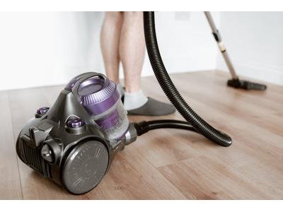 A person vacuuming a hardwood floor with a modern, purple and gray vacuum cleaner, highlighting the process of maintaining clean and dust-free living spaces.