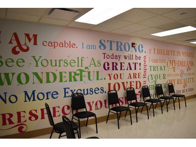 A rehab center's motivational wall filled with colorful and encouraging phrases like "I am capable," "Today will be great," and "Respect yourself," with a row of chairs lined up beneath it, creating an inspiring and supportive atmosphere for client