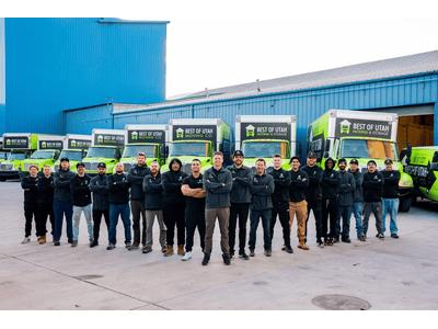 The photo features the Best of Utah Moving Co. team standing proudly in front of their bright green and black moving trucks, showcasing their readiness and professionalism. The lineup conveys a sense of unity and capability in handling moving services.