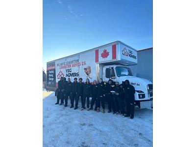 YEG Movers team standing in front of their moving truck, which features a large Canadian flag and branding for YEG Movers. The truck is parked on a snowy ground, with all team members wearing dark uniforms and smiling at the camera.