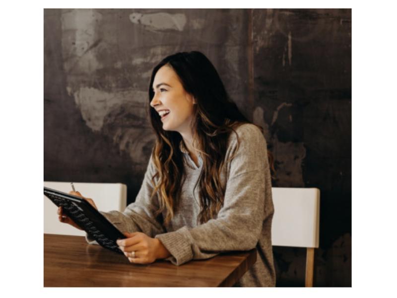 A woman sits at a table with a tablet, smiling and engaged, suggesting a productive and positive work or consultation environment.