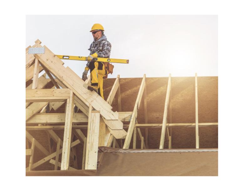 A construction worker in safety gear balances on a wooden roof frame while using a level, showcasing precision during a roofing project.