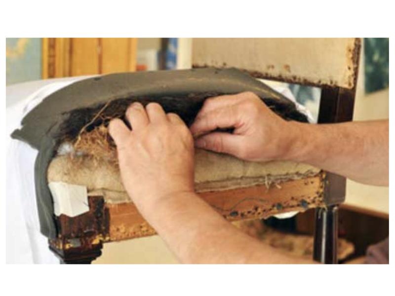 A close-up of a craftsman reupholstering an old chair, carefully restoring its worn padding and fabric.