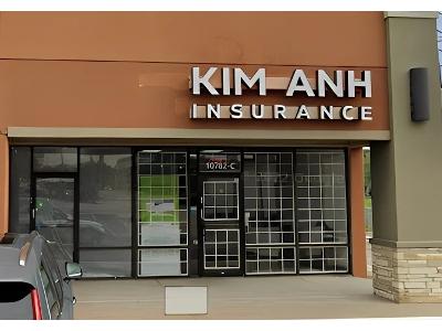 The Kim Anh Insurance office is showcased in this exterior photo, clearly identified by its large, silver signage against a warm brown-orange facade in a commercial plaza. The front is composed entirely of glass windows and doors, indicating a bright and