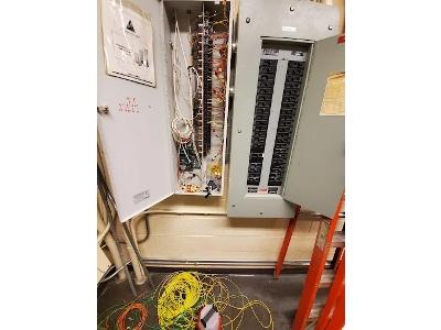 The image shows an open commercial electrical panel with exposed wiring next to a breaker panel, suggesting the photo was taken during complex wiring or repair work. Davids Electrical Services - Electrician Greensboro NC is a locally-owned company providi