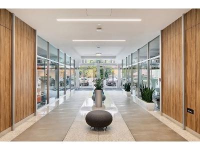 The image is a medium-close-up portrait of a distinguished man seated at a table on an outdoor rooftop terrace at sunset.
